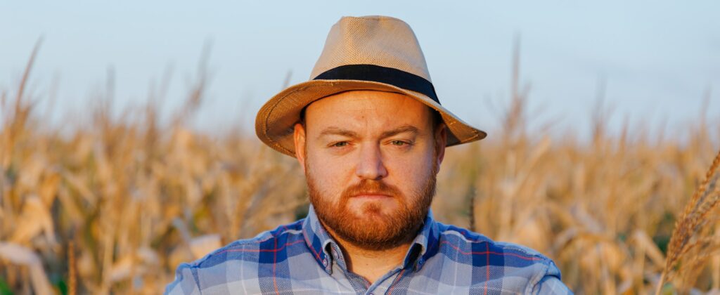 Portrait of a farmer with hat in a field of maize. Man in a rural agricultural environment.